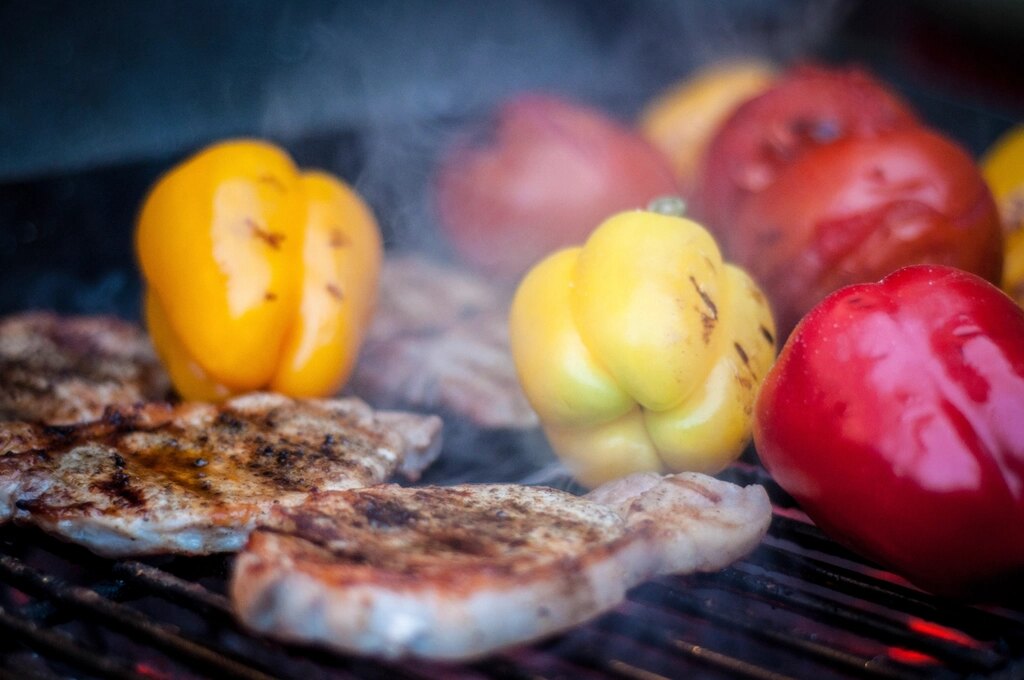 Possun kyljyksiä ja paprikoita grillin ritilällä, savu nousee.